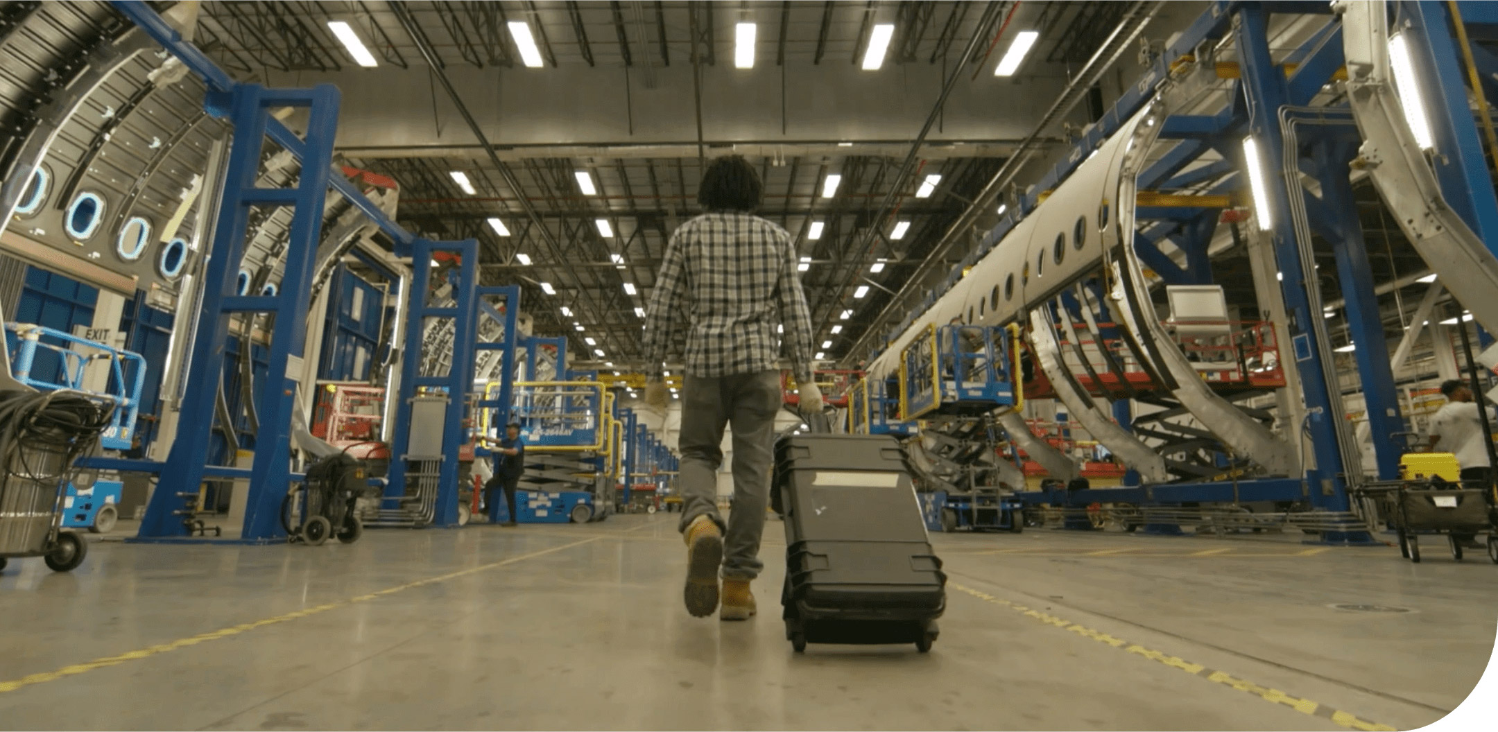 Video still of man walking away with a suitcase in an industrial warehouse.