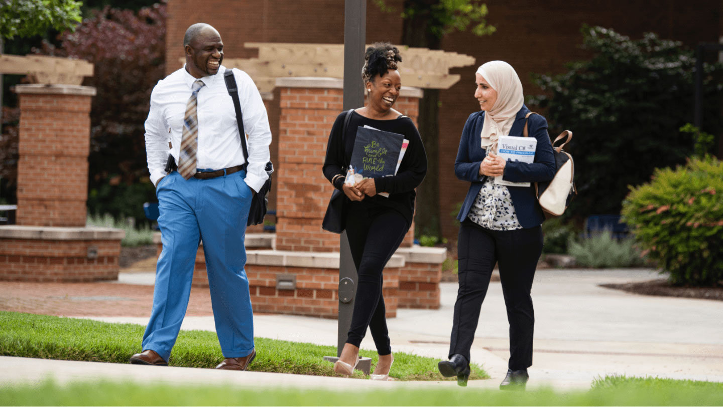Three adults walking and talking together on a school campus.